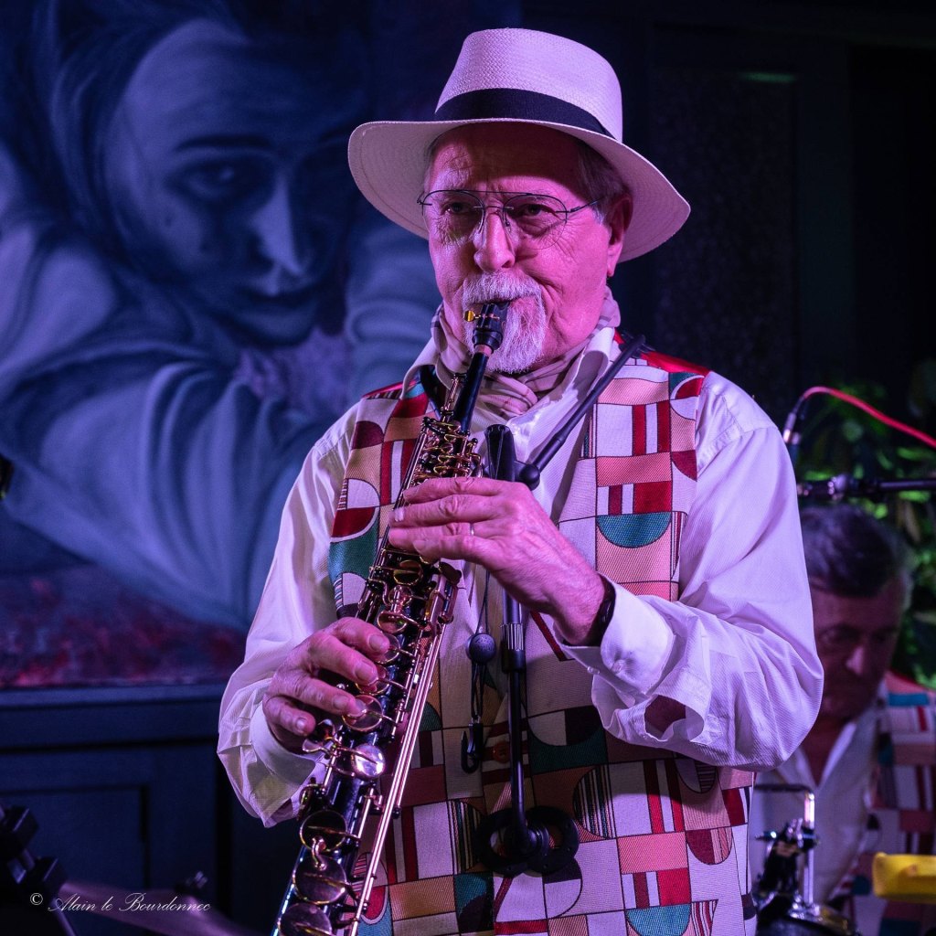 Le saxophoniste de Jazz Tico, chapeau blanc, au saxophone soprano devant une grande fresque