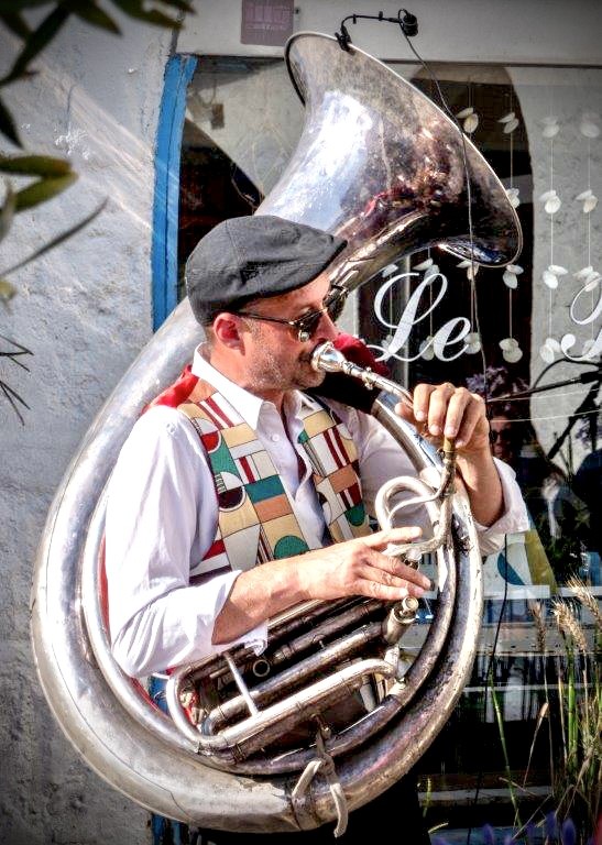 Le joueur d'hélicon de Jazz Tico, casquette et lunettes de soleil, devant une façade blanche