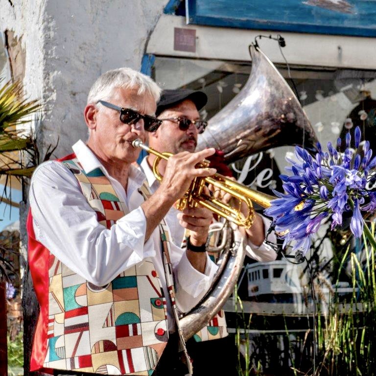 Le trompettiste de Jazz Tico joue au soleil, l'hélicon derrière lui et des agapanthes au premier plan